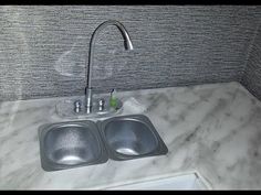 a kitchen sink and faucet with marble counter top in a corner room that has grey tile on the walls