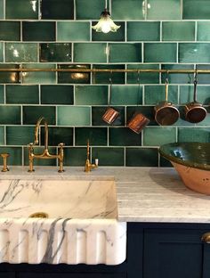 a kitchen with green tiles on the wall and copper sink faucets above it