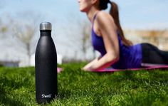 a woman laying in the grass next to a black water bottle and pink yoga mat