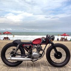 a red and black motorcycle parked on top of a brick road next to the ocean