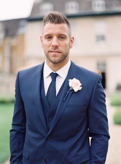 a man in a blue suit and white flower on his lapel is looking at the camera