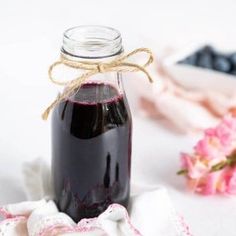 a glass jar filled with blueberries sitting on top of a white table next to pink flowers