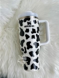 a black and white cow print travel mug on a fur rug with the words stanley printed on it