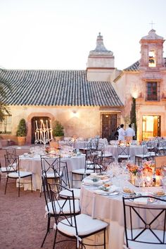 an outdoor dining area with tables, chairs and white linens set up in front of a building