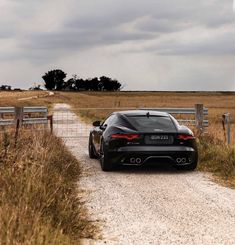 a black sports car driving down a dirt road next to a fenced in field