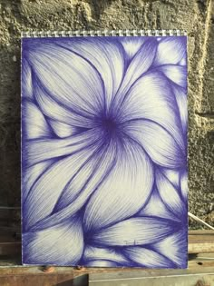 a blue and white spiral notebook sitting on top of a piece of wood next to a brick wall