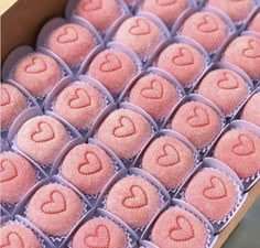 many heart shaped candies in a box with pink frosting on them and hearts drawn on the top