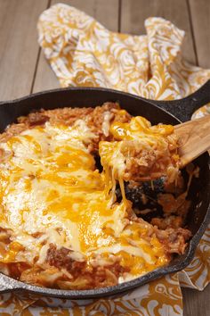 a skillet filled with cheese and meat covered in sauce on top of a table