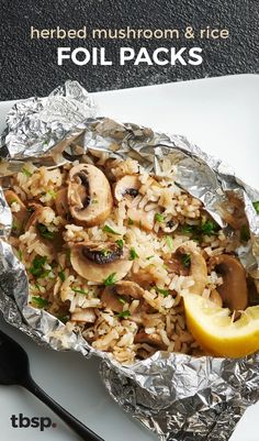 a white plate topped with foil covered in mushrooms and rice next to a lemon wedge