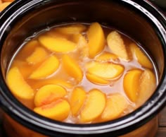 a pot filled with liquid and sliced peaches on top of a wooden table next to an orange