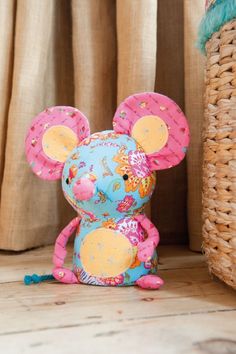 a stuffed mouse sitting on top of a wooden floor next to a wicker basket