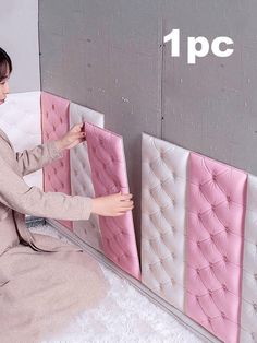 a woman sitting on top of a white bed next to a pink and gray wall