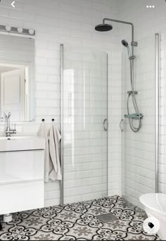 a white bathroom with black and white tile flooring, shower stall and sink area