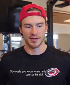 a man wearing a black shirt and red hat in a gym area with an exercise quote on it