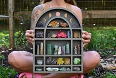 a woman sitting on the ground holding up a shelf filled with different types of rocks