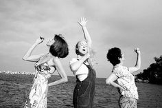 three women standing next to each other in front of the ocean with their arms up