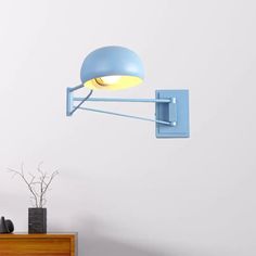 a blue wall mounted light on the side of a white wall next to a wooden dresser