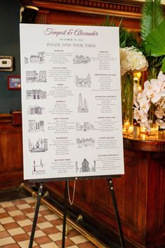 a sign on a tripod in front of a table with flowers and greenery