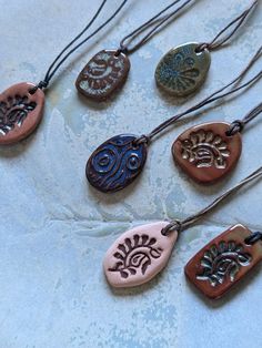 six necklaces with different designs on them sitting on a white tablecloth covered surface