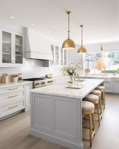 a large kitchen with white cabinets and gold pendant lights hanging from the ceiling over the island