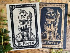 two halloween cards sitting next to each other on top of a wooden table with greenery