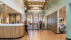 two women are standing at the front desk of a hotel lobby with wooden slats on the walls