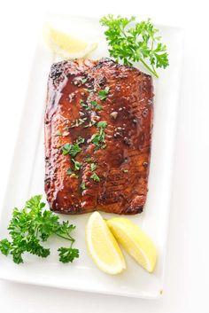 grilled salmon with lemon wedges and parsley on a white square platter