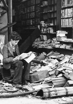 an old photo of a man sitting in front of a pile of books on the ground