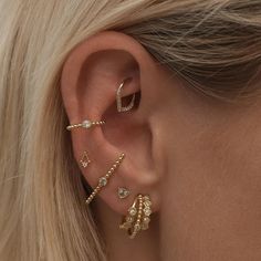 a woman wearing three different ear piercings on her left ear and the other two are gold