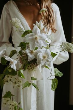 a woman wearing a white dress holding a bouquet of flowers and greenery in her hands