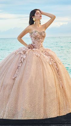 a woman in a ball gown standing by the ocean with her hand on her head