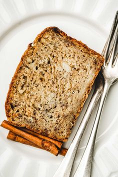 a piece of bread and cinnamon sticks on a white plate with silver utensils