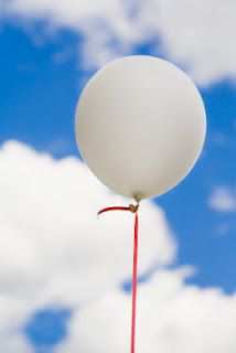 a white balloon floating in the air with a red stick sticking out of it's side