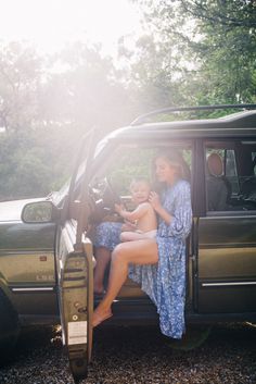 a woman sitting in the driver's seat of a car with a baby on her lap