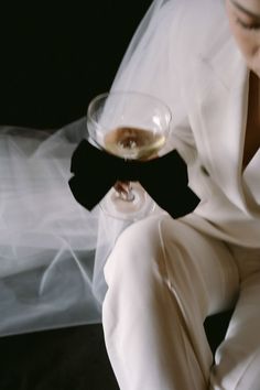 a woman in a white suit holding a wine glass and wearing a black bow tie