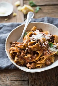 a white bowl filled with pasta and meat covered in parmesan cheese on top of a wooden table