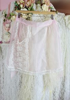 a white skirt hanging on a rack with pink flowers and other things around it in front of a pink wall