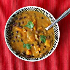 a white bowl filled with black bean and potato soup on top of a red cloth