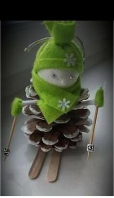 a green stuffed animal sitting on top of a pile of pine cones and holding skis