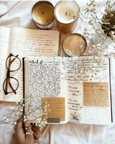 an open book sitting on top of a bed next to two glasses and flowers in front of it