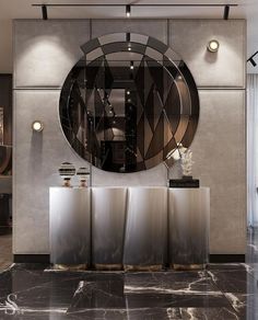 a large round mirror on the wall above two metal urns in front of a black marble floor