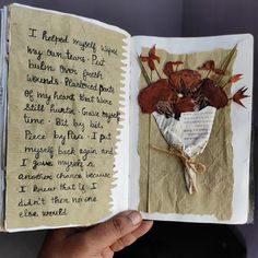 an open book with writing on it in someone's hand and some dried flowers