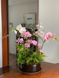 a potted plant with pink and white flowers on a table in front of a mirror