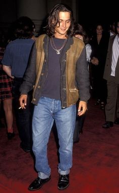 a man with long hair standing on a red carpet wearing jeans and a leather jacket