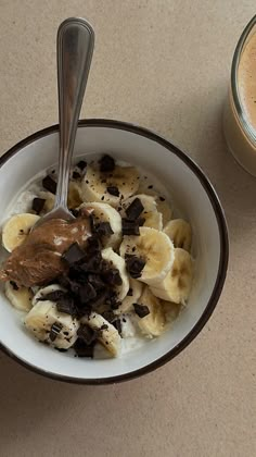 a bowl of food with chocolate chips and bananas in it next to a cup of coffee