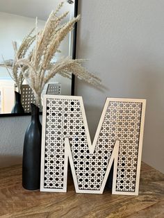 the letter m is made out of laser cut paper and sits on a table next to a vase with flowers