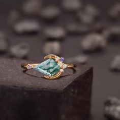 a gold ring with an aqua blue stone and two white diamonds on the side, sitting on top of a rock