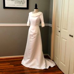 a white wedding dress is on display in front of a gray wall and wooden floor