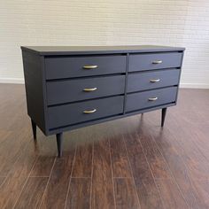 a black dresser with gold handles and drawers on it's sides, against a white brick wall