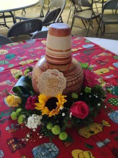 a table topped with a cake and flowers on top of a red cloth covered table